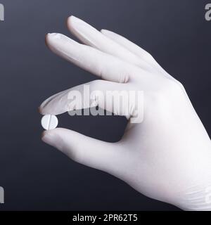 Handschuhe in der Hand, die eine Pille hält Stockfoto