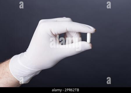 Handschuhe in der Hand, die eine Kapsel hält Stockfoto
