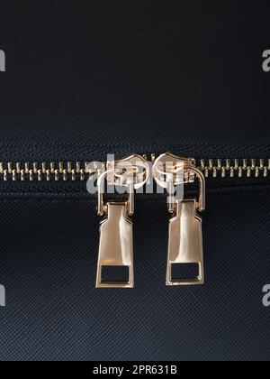 goldene Reißverschlüsse mit goldenen Reißverschlüssen sind auf einem schwarzen Lederobjekt aus der Nähe befestigt Stockfoto