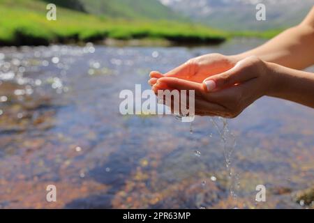 Geschwungene Frauenhände, die Wasser in einem Fluss fangen Stockfoto