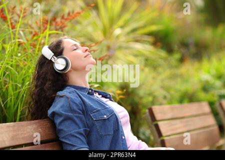 Entspannte Frau, die in einem Park Musik hört Stockfoto