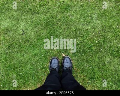 Zwei schwarze Schuhe und Beine auf einer Grasfläche – Konzept mit Draufsicht. Stockfoto