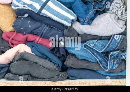 Chaotische Garderobe und schlampiger Kleiderschrank zeigen viele Outfits einer Frau mit Einkaufssucht und viele Kleidung wie Pullover, Hemden und Hosen als zerknitterte Wäsche, die in einem dreckigen Haufen Mode gelagert wird Stockfoto