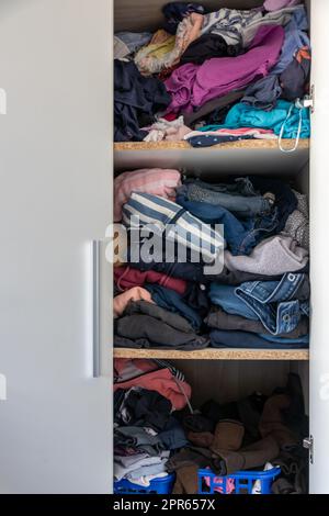 Chaotische Garderobe und schlampiger Kleiderschrank zeigen viele Outfits einer Frau mit Einkaufssucht und viele Kleidung wie Pullover, Hemden und Hosen als zerknitterte Wäsche, die in einem dreckigen Haufen Mode gelagert wird Stockfoto