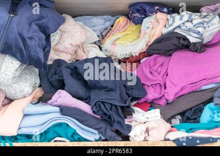 Chaotische Garderobe und schlampiger Kleiderschrank zeigen viele Outfits einer Frau mit Einkaufssucht und viele Kleidung wie Pullover, Hemden und Hosen als zerknitterte Wäsche, die in einem dreckigen Haufen Mode gelagert wird Stockfoto