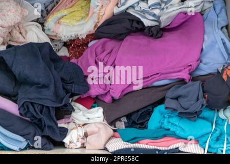 Chaotische Garderobe und schlampiger Kleiderschrank zeigen viele Outfits einer Frau mit Einkaufssucht und viele Kleidung wie Pullover, Hemden und Hosen als zerknitterte Wäsche, die in einem dreckigen Haufen Mode gelagert wird Stockfoto