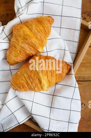 Frühstück im Bett, frische Croissants und eine Tasse Kaffee auf einem Holztablett. Guten Morgen. Stockfoto