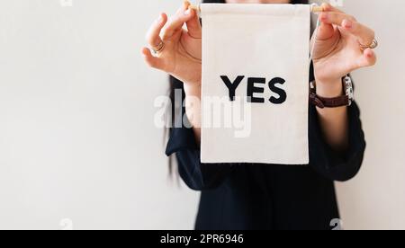 Junge Geschäftsfrau in einem schwarzen Anzug zeigt eine weiße Plakatwand auf einem weißen, isolierten Hintergrund. Auf dem Poster steht ja. Konzept für Unternehmen und Werbung. Banner. Stockfoto