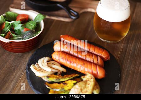 Würstchen und gegrilltes Gemüse mit einem Glas Bier Stockfoto