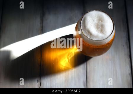 Ein schäumendes Bier, das in ein kurzes, abgerundetes Glas gegossen wurde, erstrahlt vom starken Nachmittagslicht Stockfoto