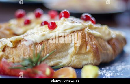 Frisch gebackene Croissants mit weißer, weicher und süßer Sahne und roten Beeren auf einem Teller. Kontinentales Frühstück mit zwei köstlichen Croissants mit Sahne auf einem Tag Stockfoto