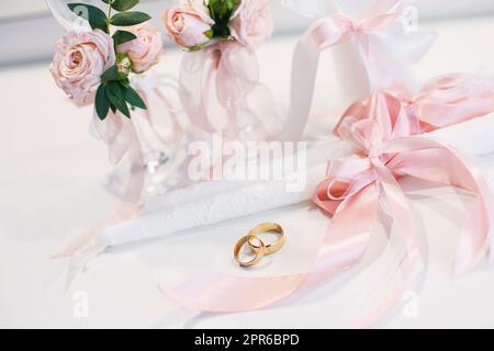 Goldene Eheringe liegen auf dem Tisch neben den Hochzeitskerzen. Stockfoto