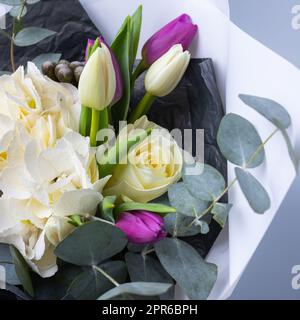 Nahaufnahme eines halben Straußes aus Tulpen, weißen Hortensien und Eukalyptuszweigen auf blauem Hintergrund. Stockfoto