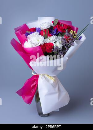 Bouquet von rosa und weißen Blumen in floralem Papier auf blauem Hintergrund gewickelt. Stockfoto