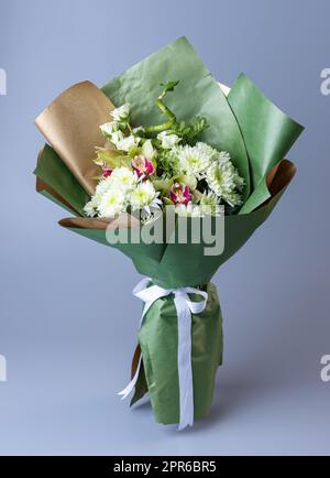 Origineller wunderschöner Strauß mit weißen Chrysanthemen, Eustoma und grünen Zweigen. Stockfoto