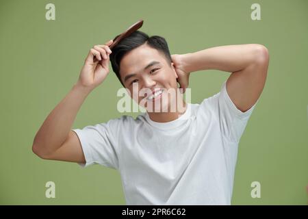 Lächelnder junger Mann, der Haare mit Kamm auf weißem Hintergrund putzt Stockfoto