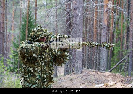 Ein Scharfschütze im Tarnanzug blickt auf das Ziel im Wald Stockfoto