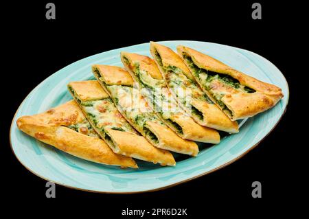 Türkische Pizza Pide mit Spinat und Käse liegt auf einem Teller auf einem schwarzen isolierten Hintergrund Stockfoto