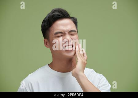 Ein hübscher junger Mann, der an Zahnschmerzen leidet. Er berührt seine Wange, um Schmerzen zu stoppen Stockfoto