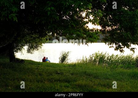 Glückliches Seniorenpaar, das im Sommer in der Nähe des Sees bei Sonnenuntergang saß Stockfoto