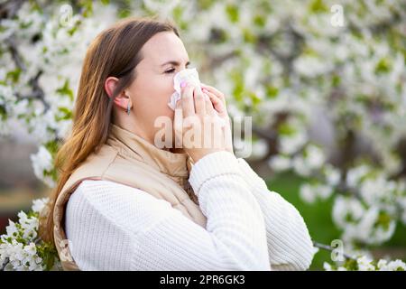 Niesende Frau mit einem Nasenwischer unter den blühenden Bäumen im Park Stockfoto