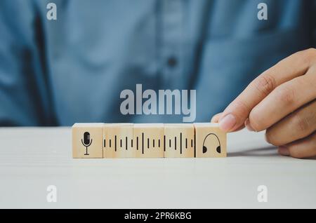 Hand setzen Holzwürfel mit Podcast-Mikrofon und Kopfhörer-Symbol auf Tisch und kopieren Raum.Geschäftskonzepte. Stockfoto