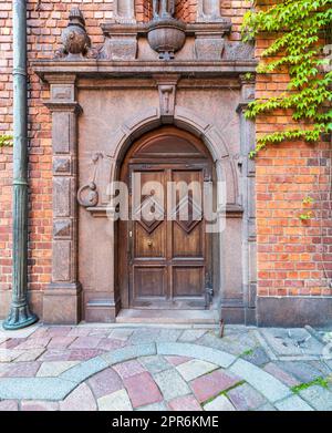 Dekorative Bogentür aus Holz, eingerahmt von eingravierten Marmor an einer roten Backsteinwand und farbenfrohem Kopfsteinfliesenboden Stockfoto