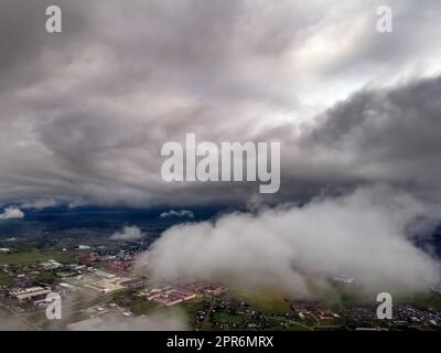 Fliegen durch dicke Wolken. Regenwolken am Himmel. Kumuluswolken, Meteorologie und Klimastudien. Foto der Stadt aus der Höhe der Wolken, Luftaufnahmen. Quadcopter, Drohne Stockfoto