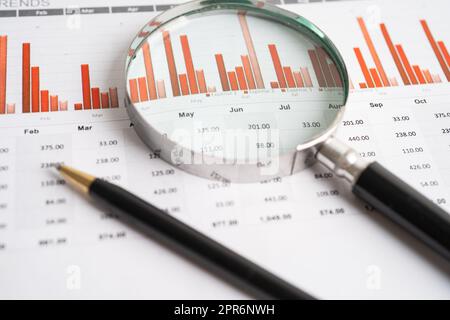 Vergrößerungsglas auf Tabellenkalkulationspapier für Diagramme. Finanzentwicklung, Bankkonto, Statistik, Wirtschaft, Börsenhandel, Meeting-Konzept für Geschäftsbüros. Stockfoto