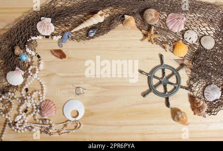 Captains Wheel mit Fischernetz und Meeresmuscheln auf Holzhintergrund Stockfoto