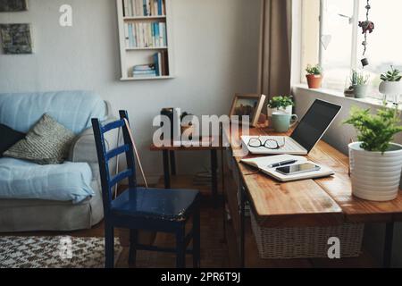 Willkommen in meinem Home Office. Eine kurze Aufnahme von Technologie und einem Notebook auf einem Schreibtisch in einem leeren Heimbüro während des Tages. Stockfoto