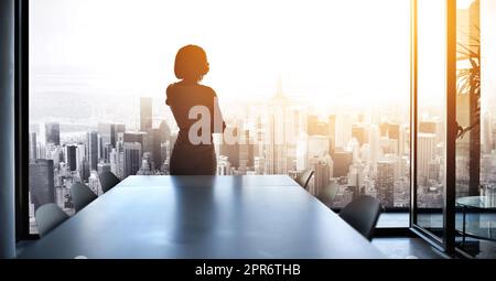 Bald werde ich diese Stadt führen. Rückansicht einer jungen Geschäftsfrau, die aus einem großen Fenster im Büro herausschaut. Stockfoto