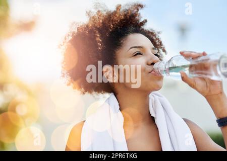 Die Aufrechterhaltung einer guten Flüssigkeitszufuhr unterstützt auch eine gesunde Gewichtsabnahme. Eine kurze Aufnahme einer jungen Frau, die beim Laufen eine Flasche Wasser genießt. Stockfoto