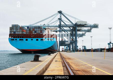 Ladungsverladung. Ein massives Frachtschiff, das am Hafen festgemacht wurde, wurde mit Containern beladen. Stockfoto