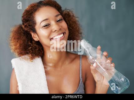 Es gibt nichts ganz wie ein gutes, solides Training. Studioportrait einer jungen Frau, die nach dem Yoga-Kurs etwas Wasser trinkt, vor grauem Hintergrund. Stockfoto