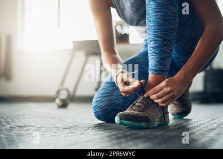 Die richtigen Schuhe machen den Unterschied aus. Aufnahme einer Frau, die ihre Schnürsenkel in einem Fitnessstudio bindet. Stockfoto