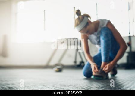 Jetzt ist es an der Zeit, sich fit zu machen. Unschärfende Aufnahme einer Frau, die ihre Schnürsenkel in einem Fitnessstudio bindet. Stockfoto