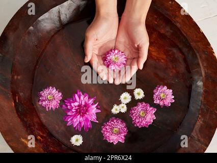 Entspannen Sie sich im Spa. Ein kurzer Schuss einer Frau reicht in einer mit Blumen gefüllten Wasserschale in einem Spa. Stockfoto