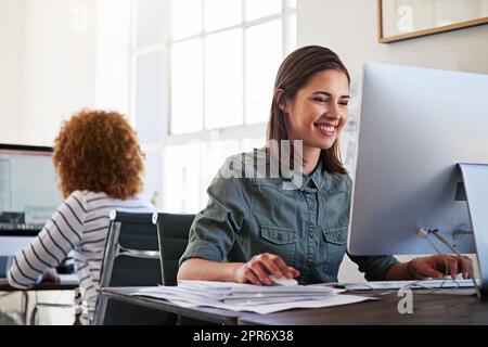 Arbeit mit einer positiven Einstellung erledigen. Aufnahme von Kollegen, die in einem Großraumbüro an ihren Computern arbeiten. Stockfoto