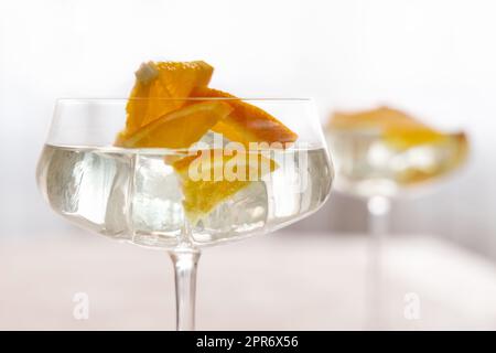Transparenter Cocktail mit Eiswürfeln in einem Glas, dekoriert mit Scheiben orangefarbener Nahaufnahmen Stockfoto
