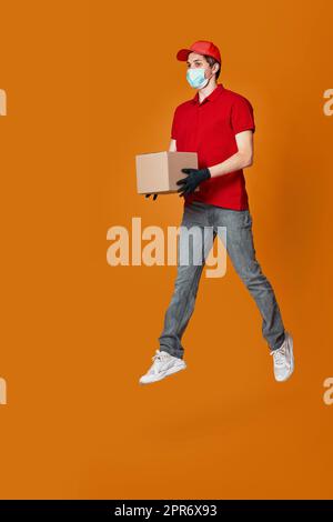 Delivery Mann in Gesichtsmaske hält Pappkarton und springen Stockfoto