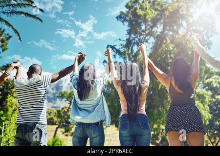 Gemeinsam erheben wir uns. Rückansicht einer Gruppe junger Freunde, die triumphierend die Hände heben. Stockfoto