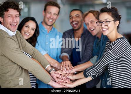 Was für ein Team. Porträt einer glücklichen Gruppe von Mitarbeitern, die ihre Hände in Einheit zusammenhalten. Stockfoto