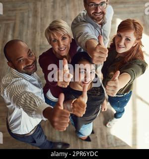 Ihr Erfolg erreicht neue Höhen. Hochwinkelporträt eines Teams von Kollegen, die in einem modernen Büro Daumen nach oben geben. Stockfoto