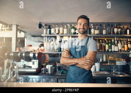 Es gibt einen Grund, warum meine Kunden immer wieder kommen. Porträt eines jungen Mannes, der hinter einer Theke arbeitet. Stockfoto