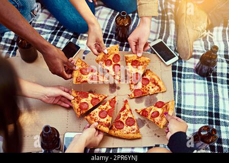 Pizza sorgt für die besten Picknicks. Kurzer Schuss einer Gruppe von Freunden, die Pizza essen, während sie ein Picknick machen. Stockfoto