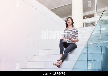 Wireless ist die intelligentere Art zu arbeiten. Porträt einer jungen Geschäftsfrau mit einem digitalen Tablet auf der Treppe in einem modernen Büro. Stockfoto