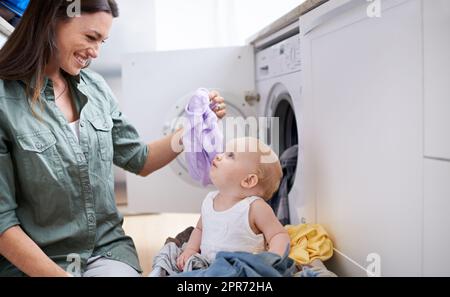 Mummys kleiner Helfer. Aufnahme einer Mutter und ihres kleinen Mädchens, die während der Wäsche spielen. Stockfoto