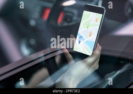 Alle möglichen Routen erkunden. Aufnahme einer Frau in einem Auto, die ein Telefon benutzt, um eine Wegbeschreibung zu finden. Stockfoto