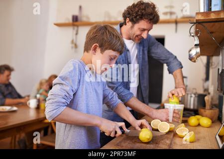 Limonade für die Familie. Ein zugeschnittenes Porträt eines glücklichen Vaters und Sohnes, der in ihrer Küche zu Hause Limonade herstellt. Stockfoto